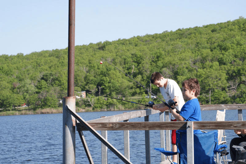 Two boys fishing on a pier near the water.