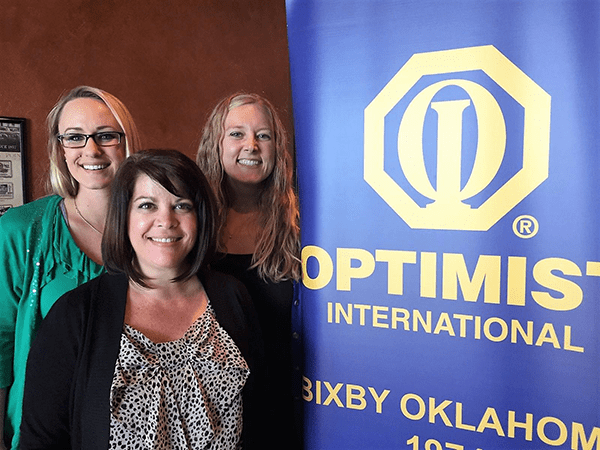 Three women standing next to a banner that says optima international.