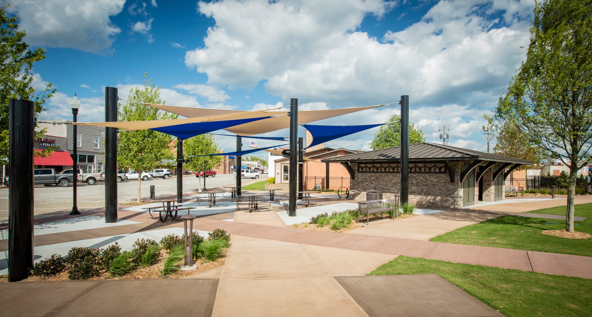 A park with benches and picnic tables under shade sails.